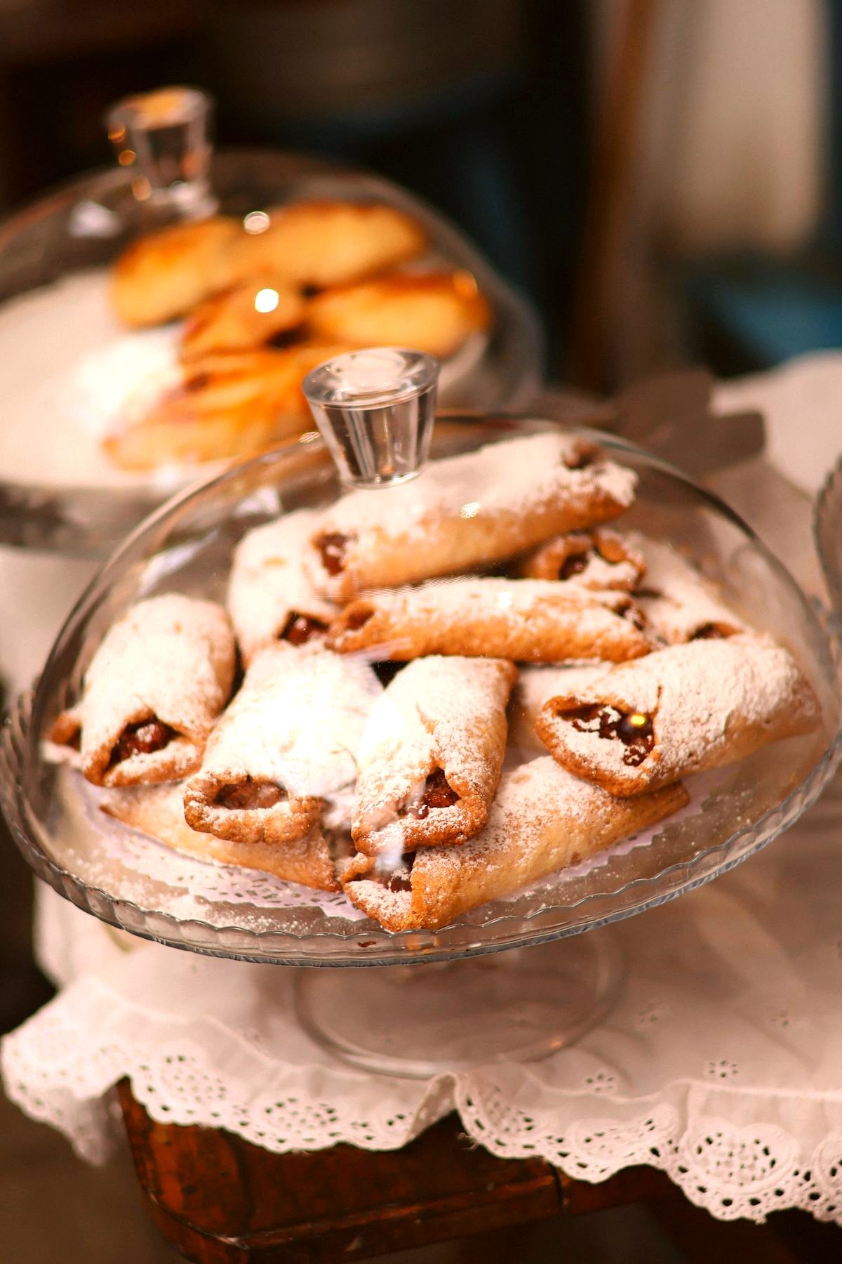 Powdered-sugar cannoli piled high under glass cake domes at an Italian bakery